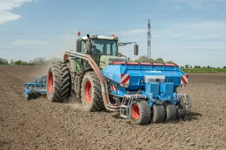 Traktor táhne modrý přední zásobník Lemken Solitair na poli.